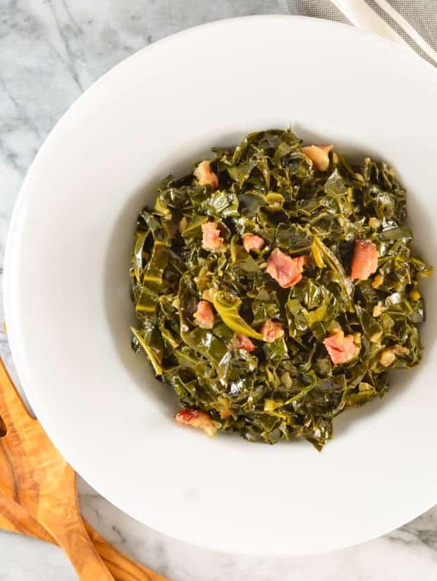 overhead of collard greens with ham hocks in a white bowl.