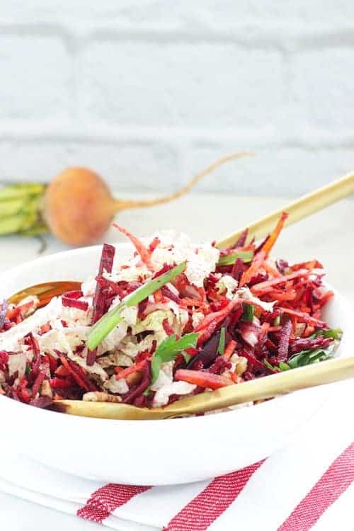 carrot and beet slaw in a white bowl with serving spoons.