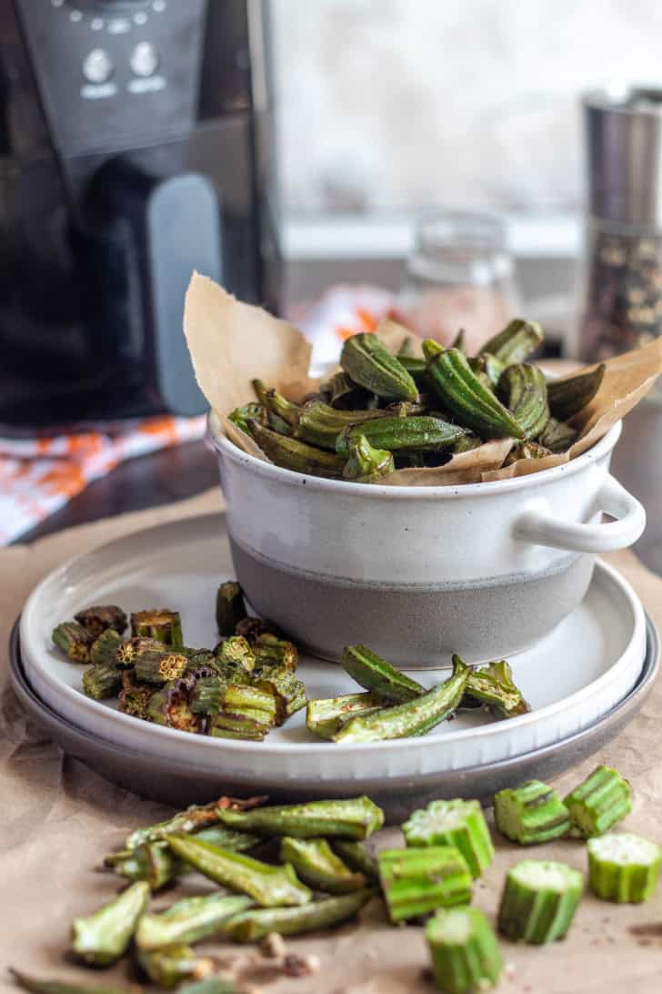 okra pieces on a piece of parchment in front of more on a plate and in a bowl.