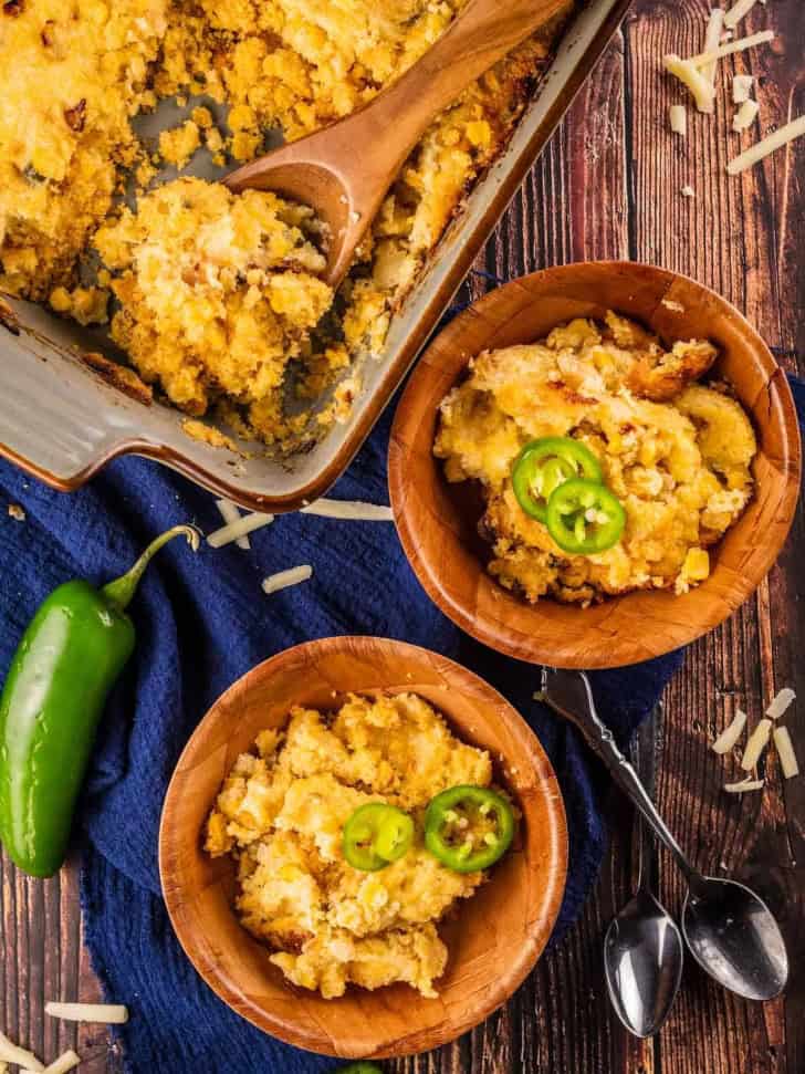 cornbread pudding in two wooden bowls with more in casserole dish next to them.