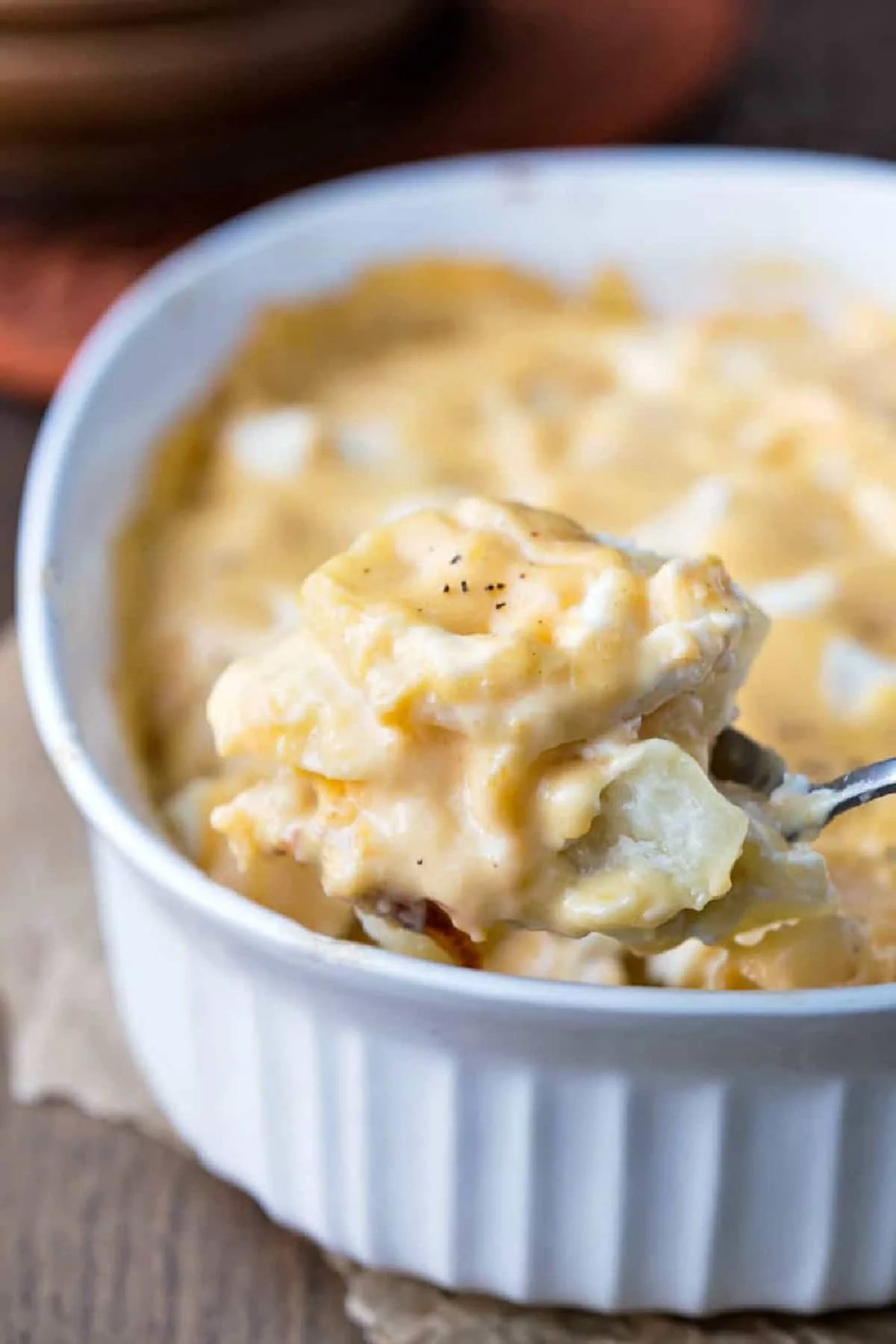 spoon scooping some scalloped potatoes from a white casserole dish.