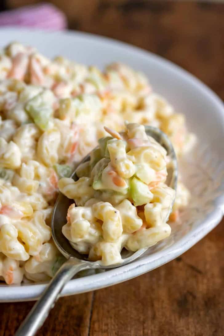 macaroni salad in a white bowl with a scoop on a spoon.