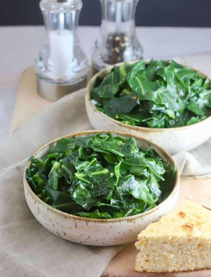 two bowls of collard greens with a piece of cornbread in the front.