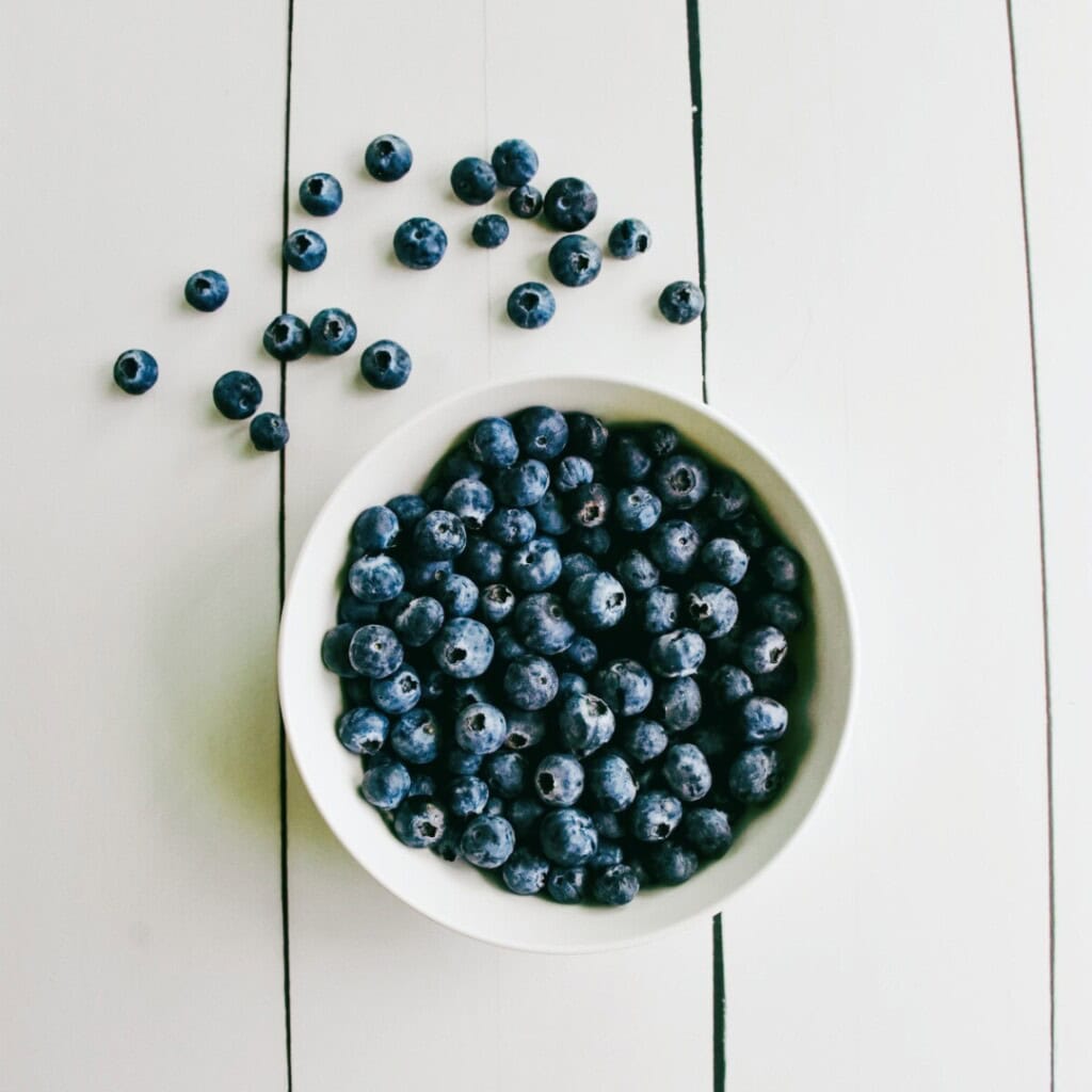 overhead shot of fresh blueberries in a white bowl with some on the table.