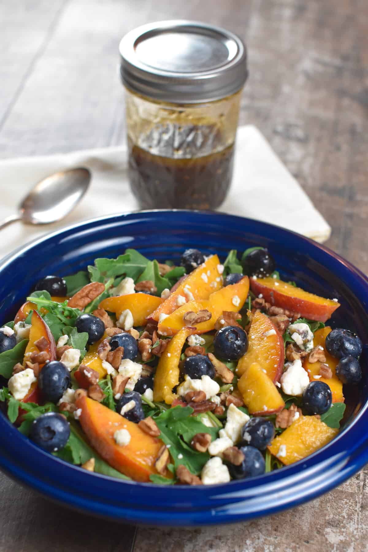 serving of arugula salad in a blue bowl with dressing behind it in a mason jar.