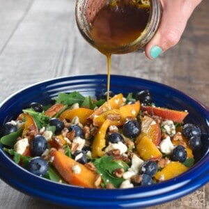 pouring balsamic dressing onto a serving of arugula salad.