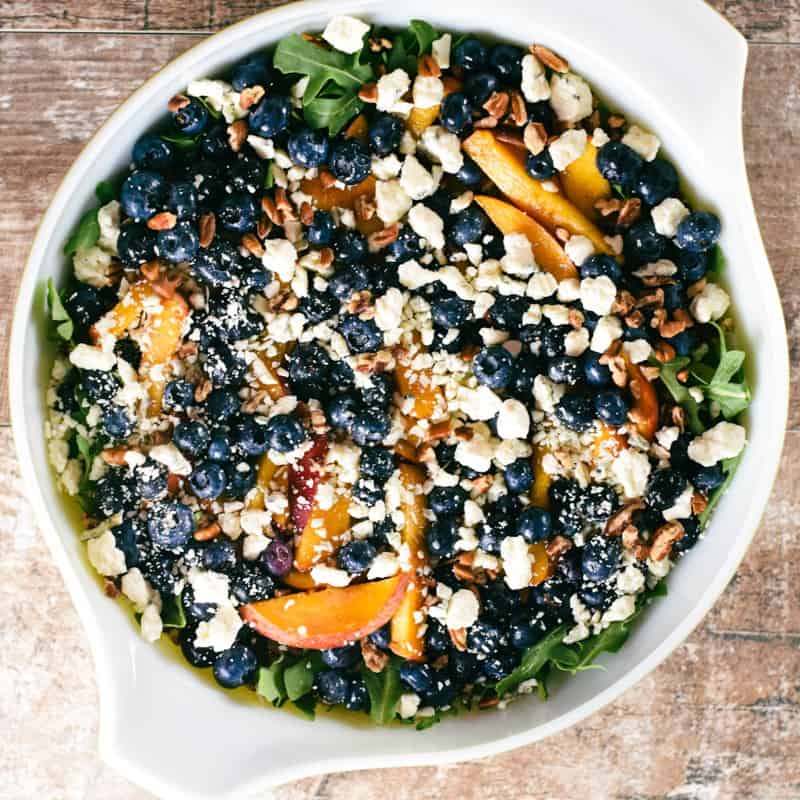 close-up overhead of blueberry and peach arugula salad in a serving bowl.