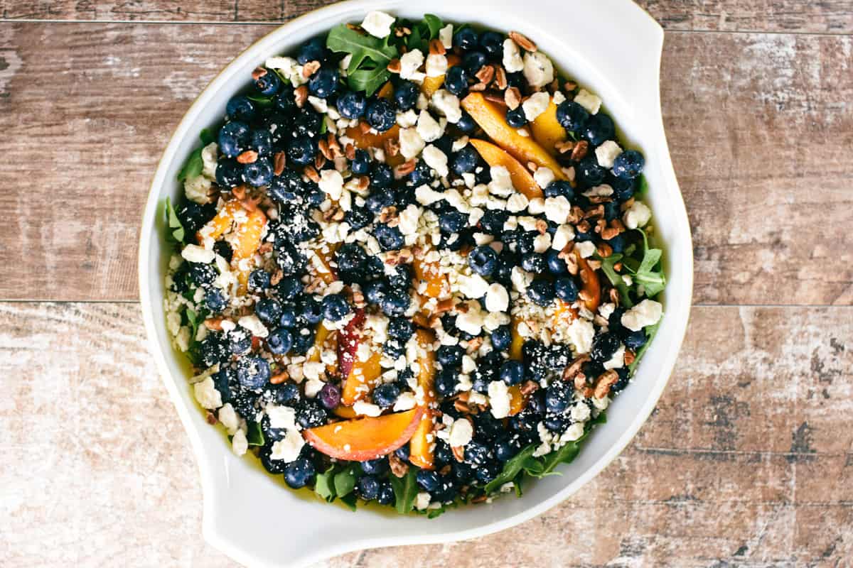 overhead of arugula salad with blueberries and peaches.