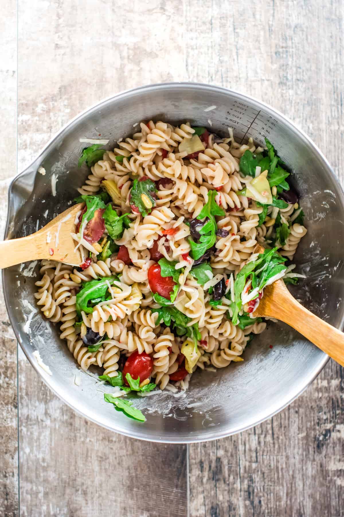 mixing pasta salad ingredients in a bowl with two spoons.