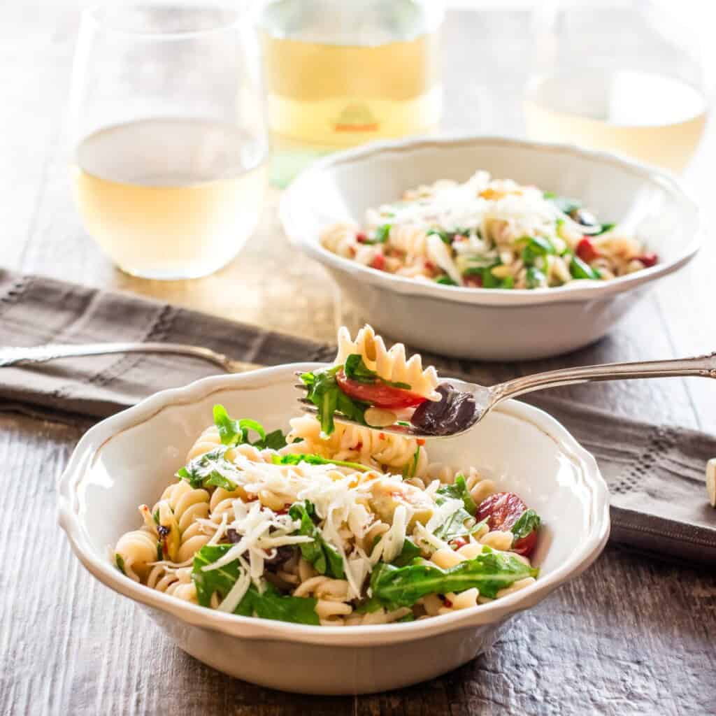 forkful of arugula pasta salad over a bowl with more and one in the background.