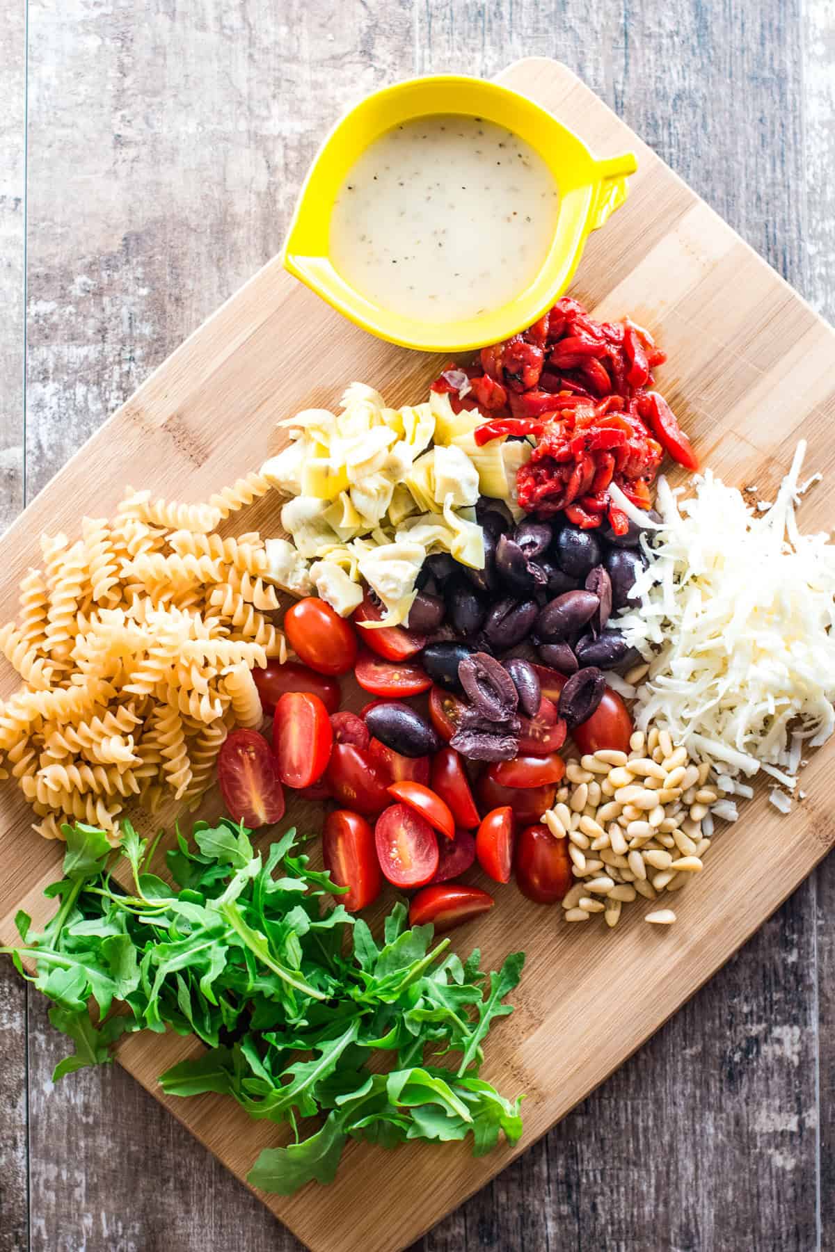 ingredients for arugula pasta salad on a wooden cutting board.