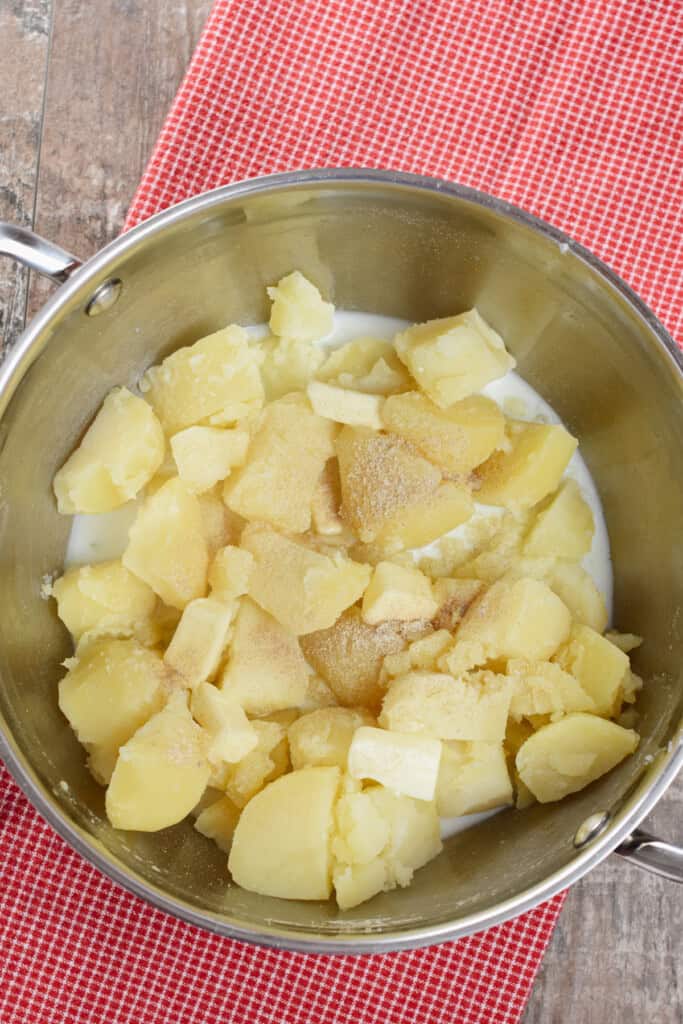 overhead of cut potatoes in a pot with milk, butter and seasonings added.