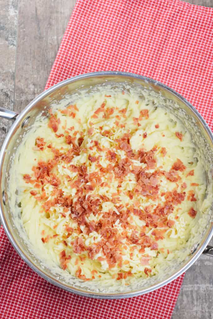 overhead shot of bacon added to the whipped mashed potatoes in a pot.