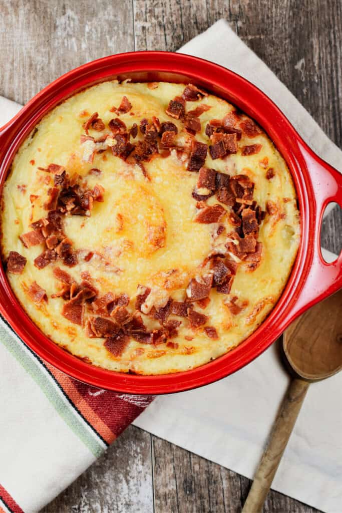 overhead of baked mashed potatoes with bacon and cheese in a red circular baking dish.