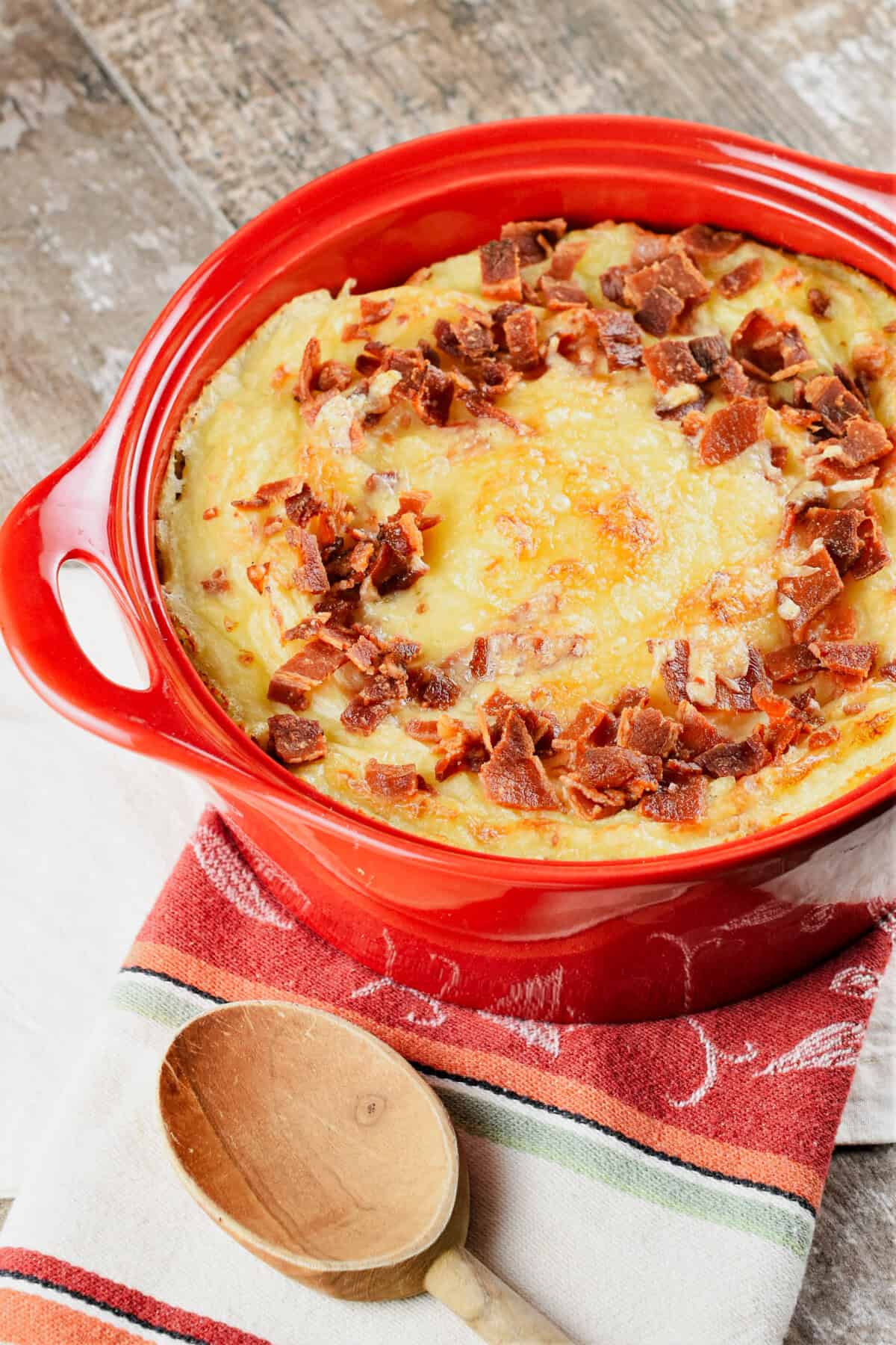 baked mashed potatoes with bacon pieces on top and cheese in a red circular baking dish.