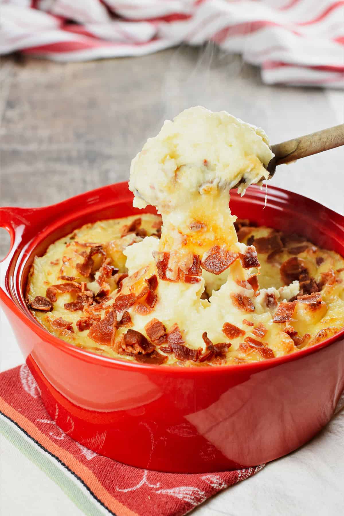 wooden spoon taking out a scoop of baked mashed potatoes from a casserole dish.