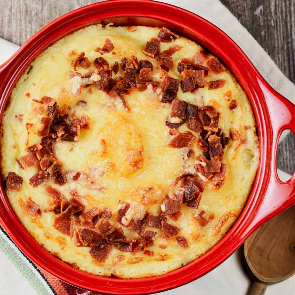 overhead close-up shot of baked mashed potatoes with bacon and cheese in a red circular casserole dish.