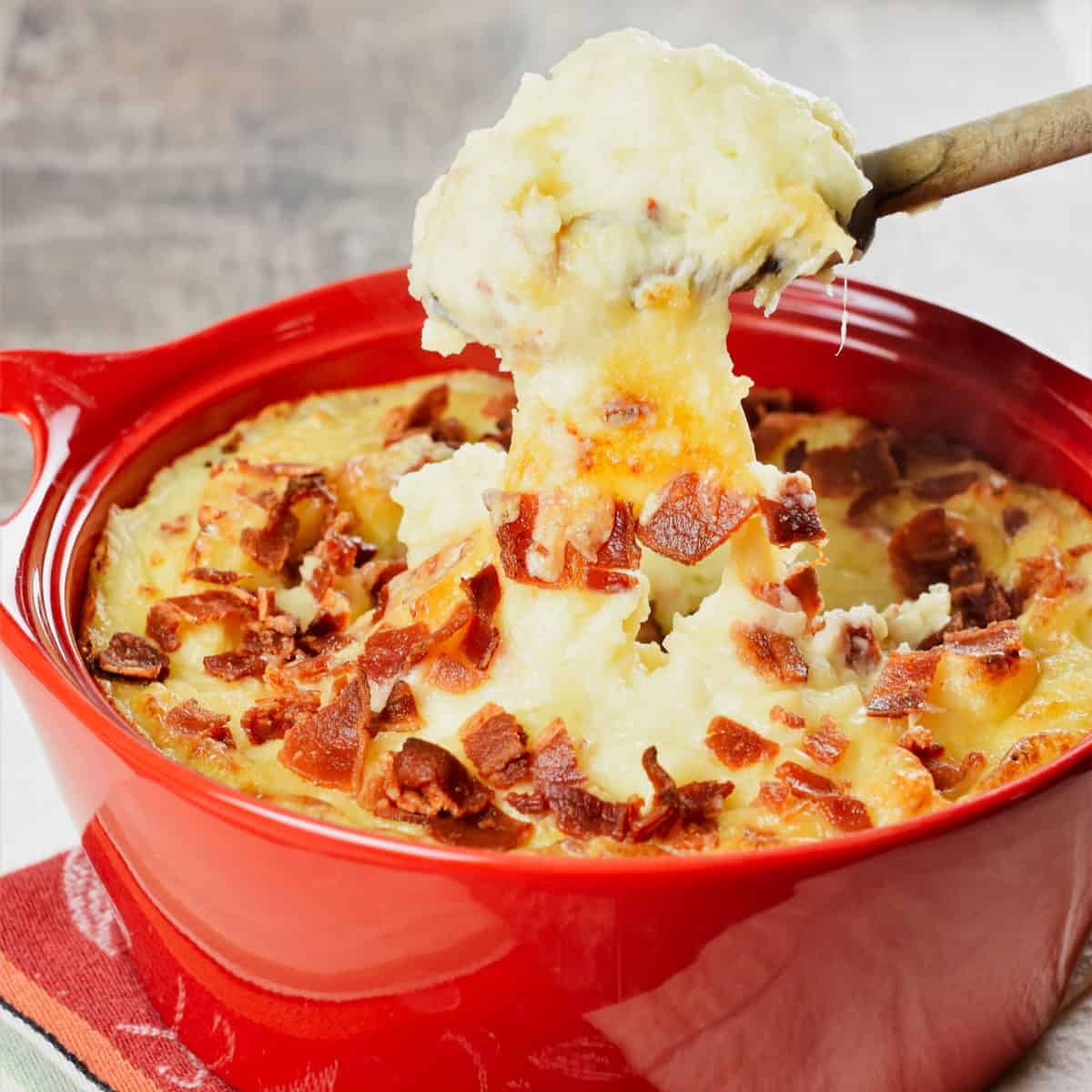 close-up shot of wooden spoon scooping out baked mashed potatoes with bacon and cheese from a casserole dish.