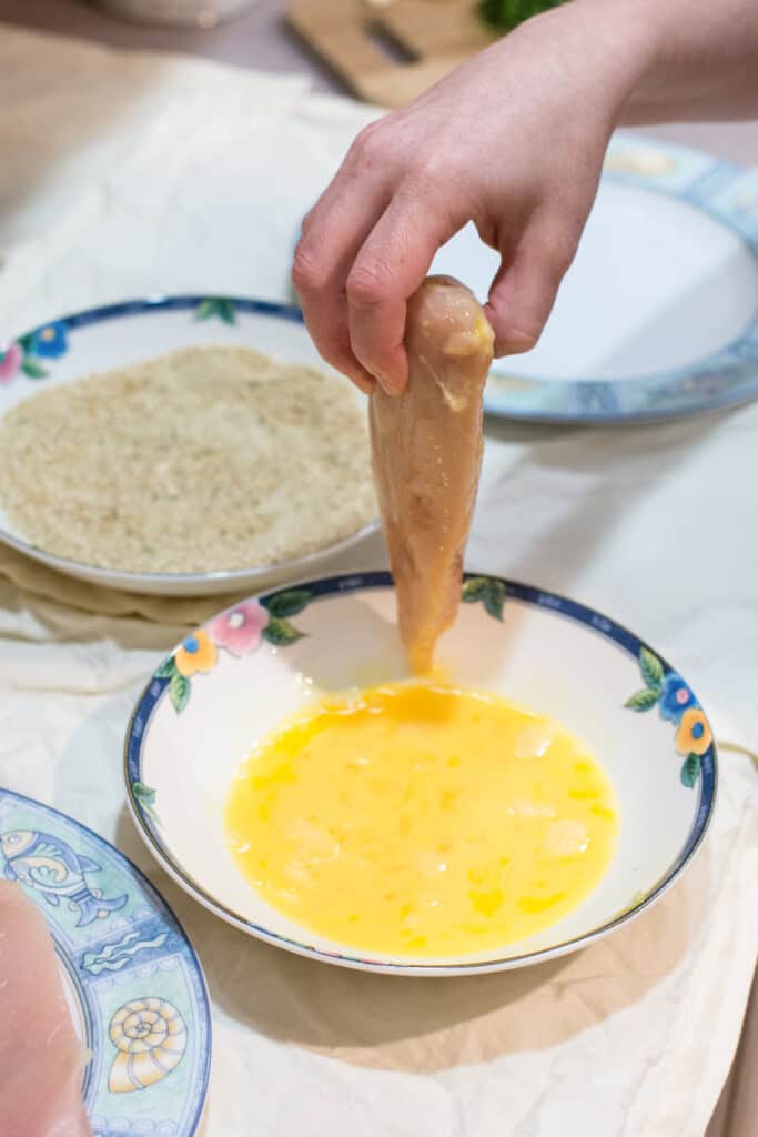 holding up chicken breast fillet after dipping in egg.