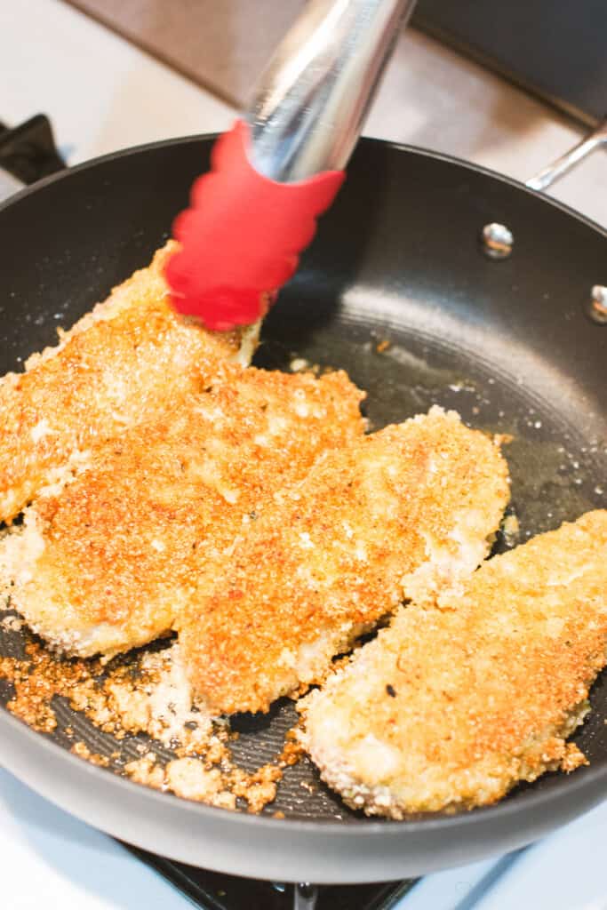 flipping a piece of breaded chicken with tongs.