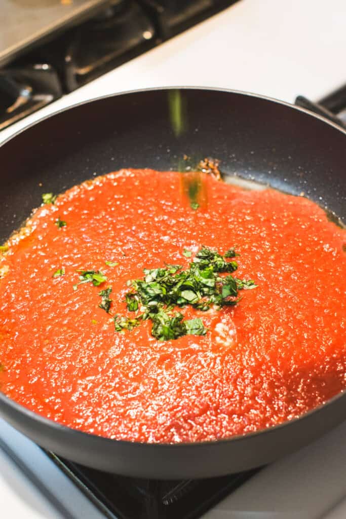 sprinkling basil into the crushed tomatoes in the skillet.