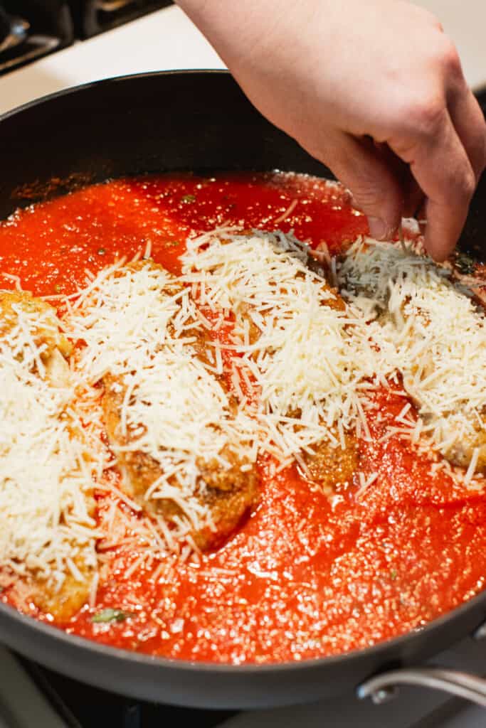 sprinkling cheese onto the chicken in the skillet.