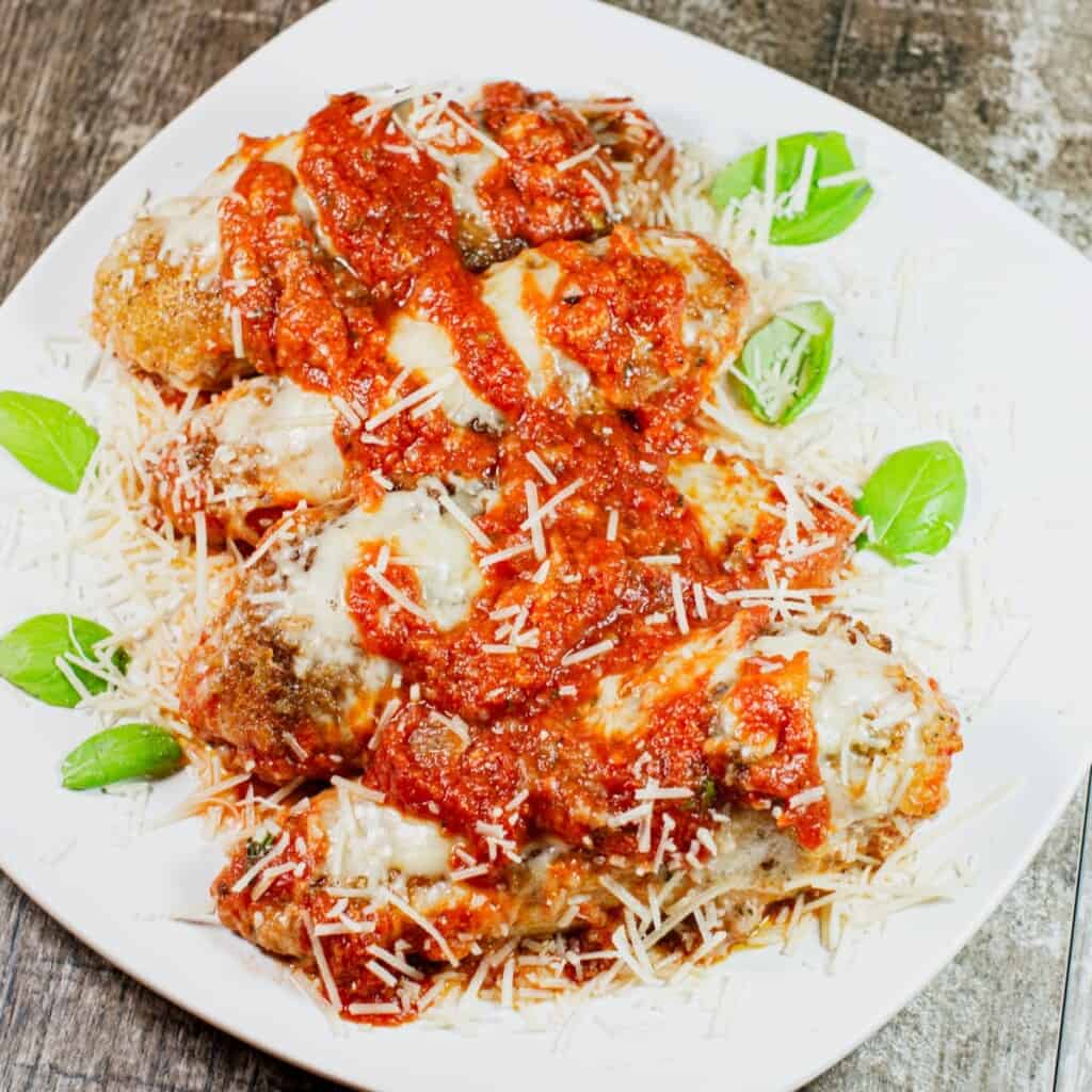 overhead shot of four pieces of skillet chicken parmesan on a white plate garnished with parmesan and basil.