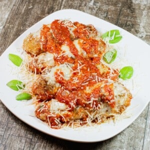 four pieces of skillet chicken parmesan on a white plate with basil garnish.