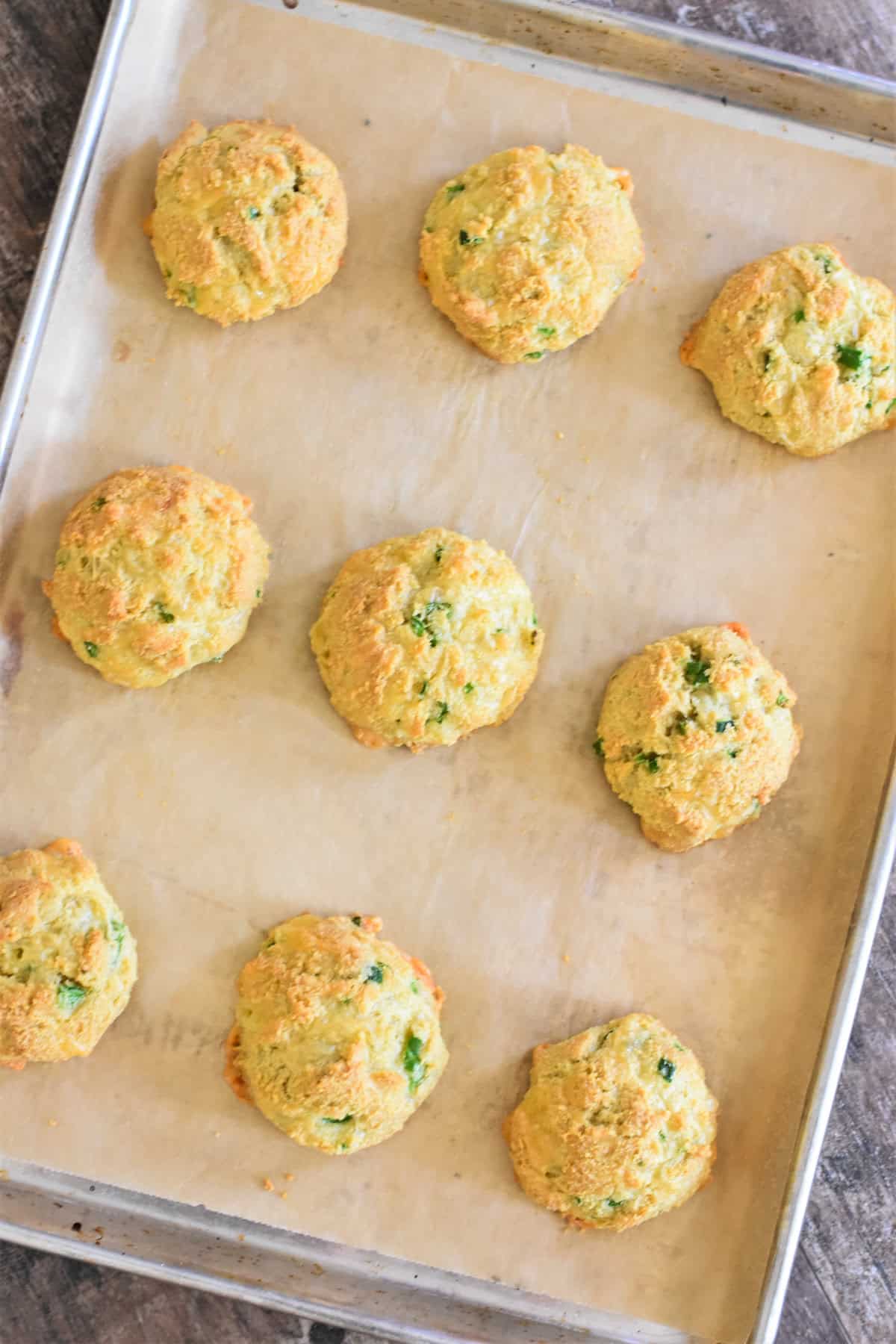 Nine almond flour biscuits on a parchment-lined tray after baking.