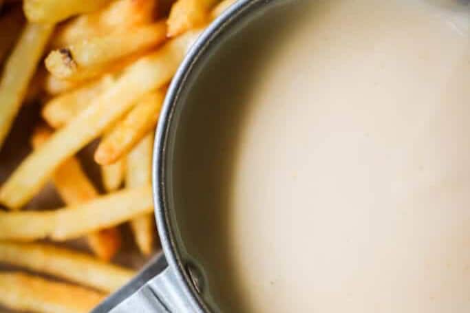 Low-carb cheese sauce in a metal cup with fries next to it.