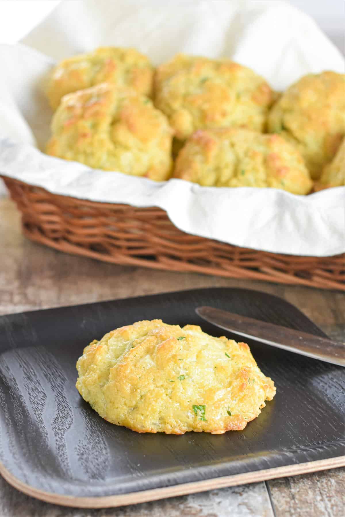 Biscuit on a plate with a knife next to it and more biscuits in a basket behind it.