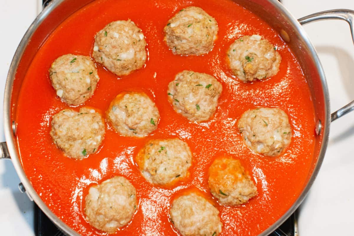 Cooked turkey meatballs floating in marinara sauce in a stainless steel skillet.