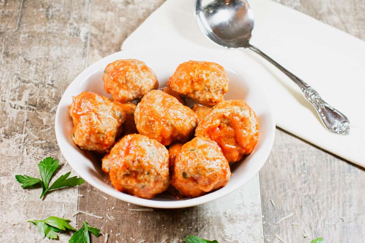 sauced turkey meatballs in a white bowl with a serving spoon next to it.