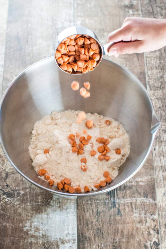 Pouring baking chips into a mixing bowl with cake mix.