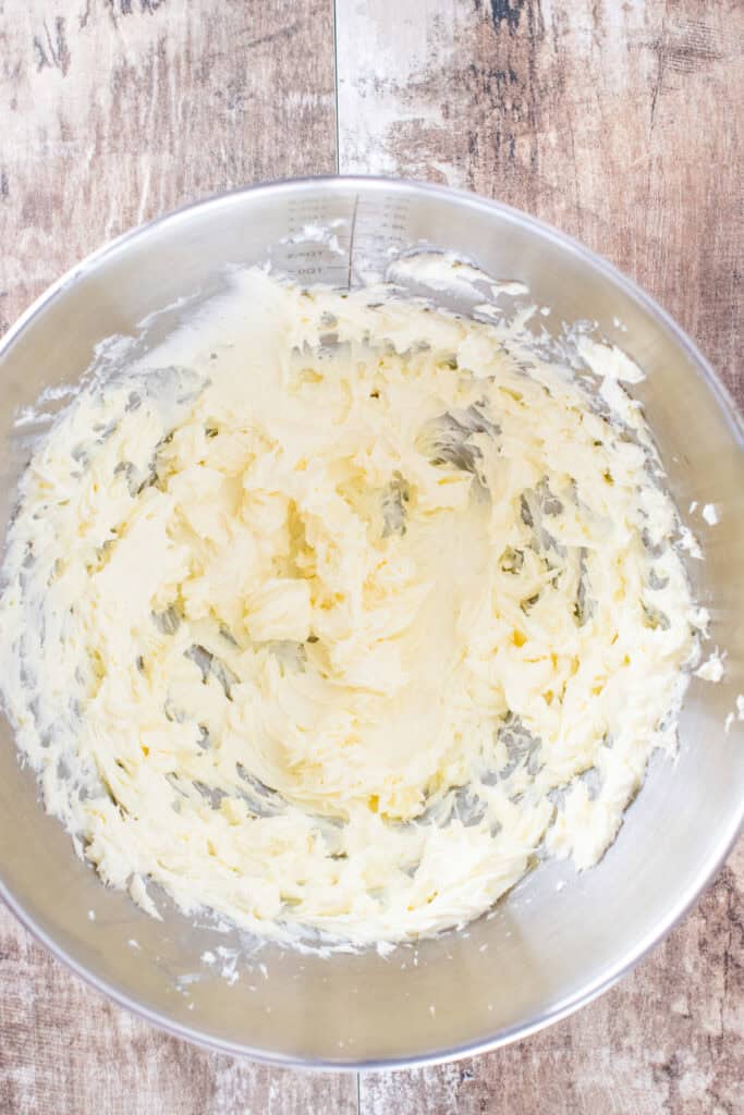 Butter and cream cheese are beaten together in a mixing bowl.