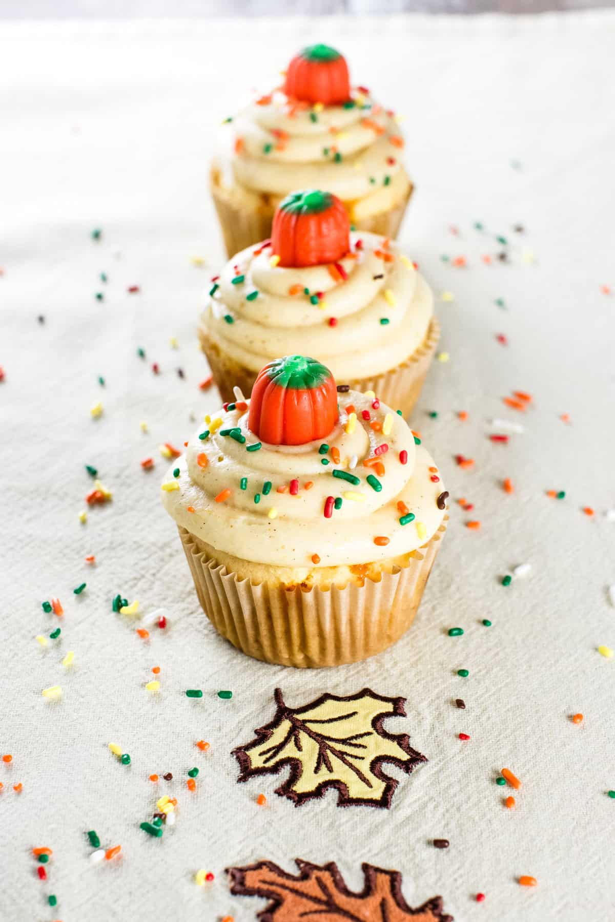 Three cake mix cupcakes with pumpkin candies on top on a kitchen napkin with a fall leaves design.