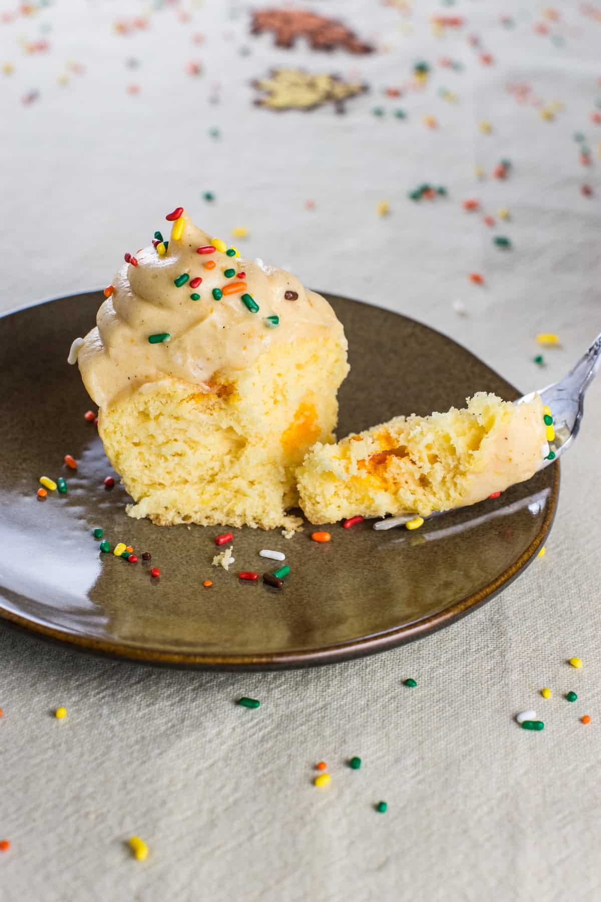 A piece of a cupcake on a fork next to the cupcake on a plate.