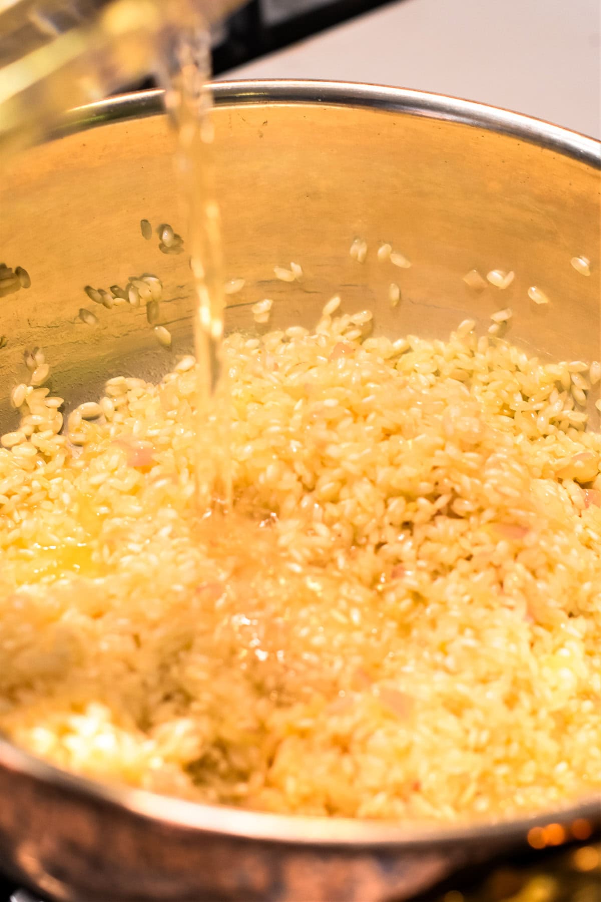 Pouring white wine into a pan with arborio rice.