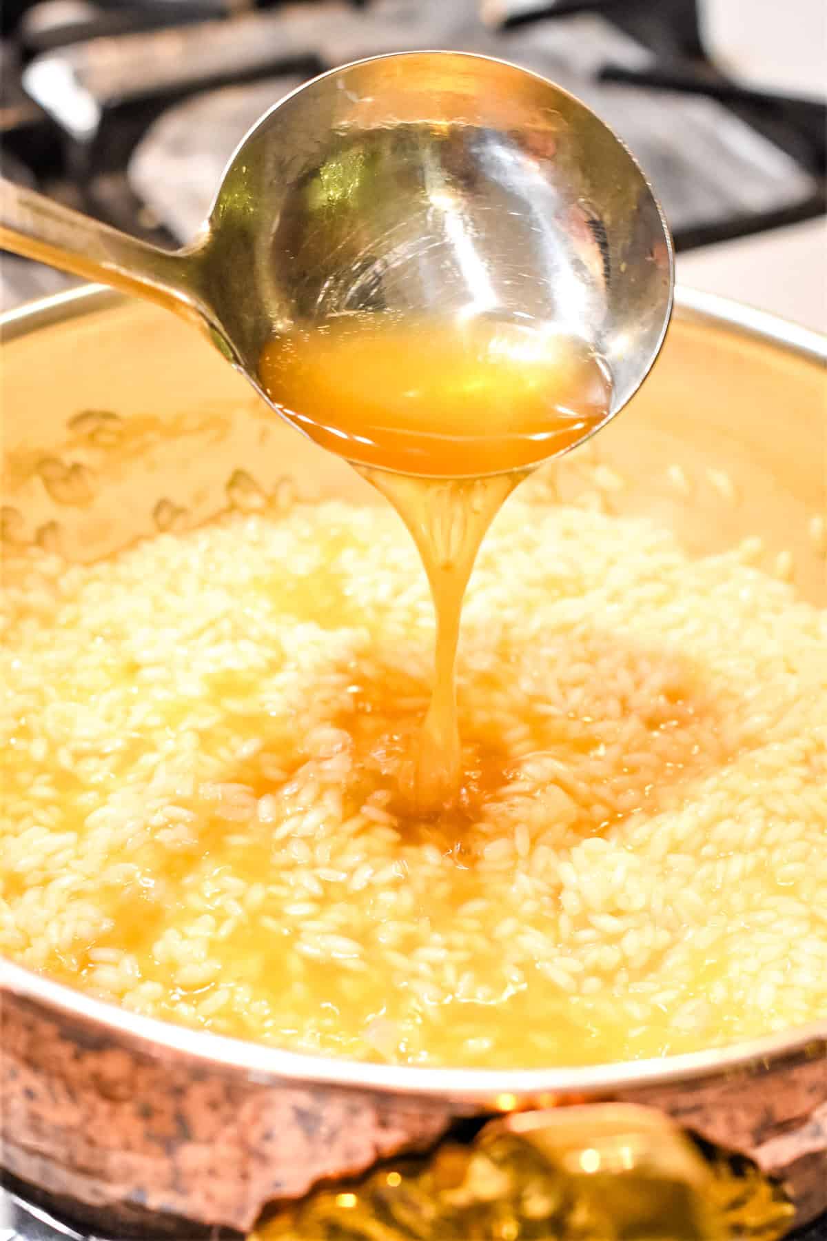 Adding a ladle of broth to risotto cooking in a pan.