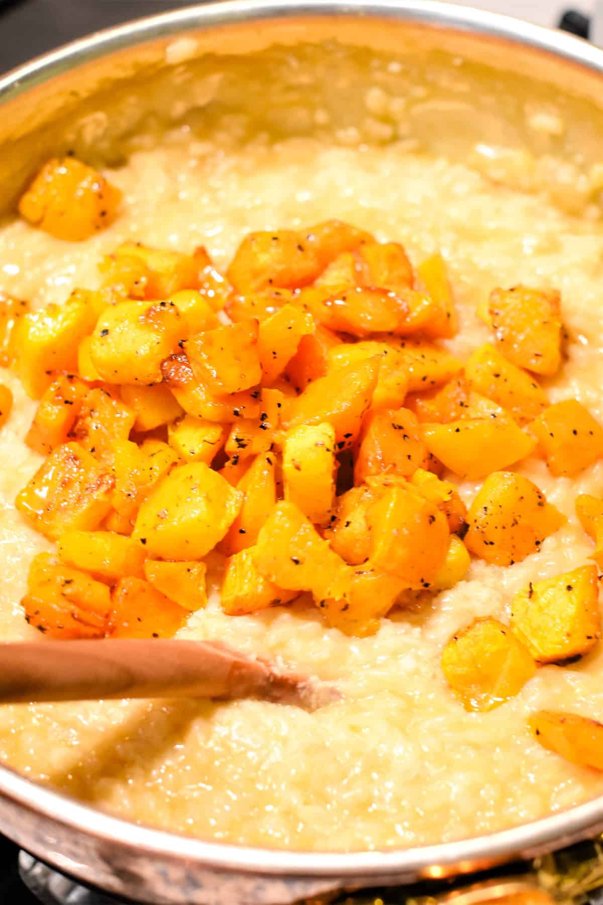 Mixing roasted butternut squash into a pan filled with risotto.