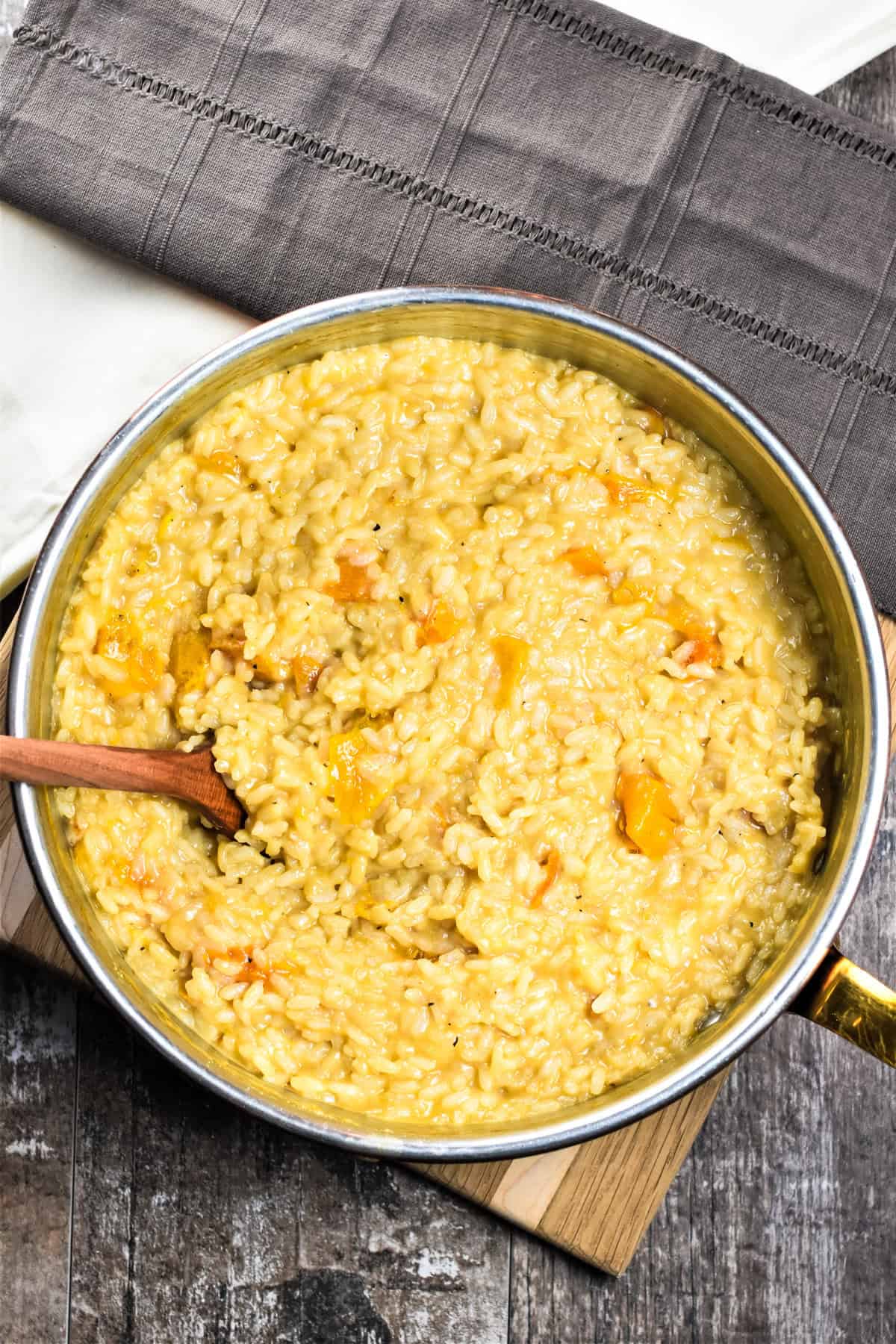 Roasted butternut squash risotto in a pan with a wooden spoon after cooking.