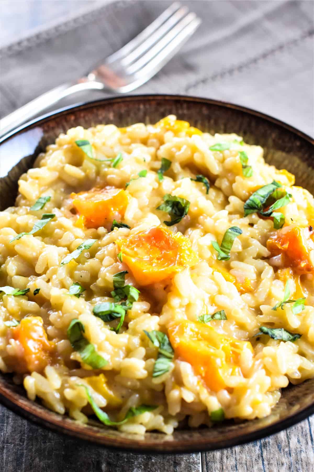 Close-up of a bowl of roasted butternut squash risotto with a fork on a kitchen napkin behind it.