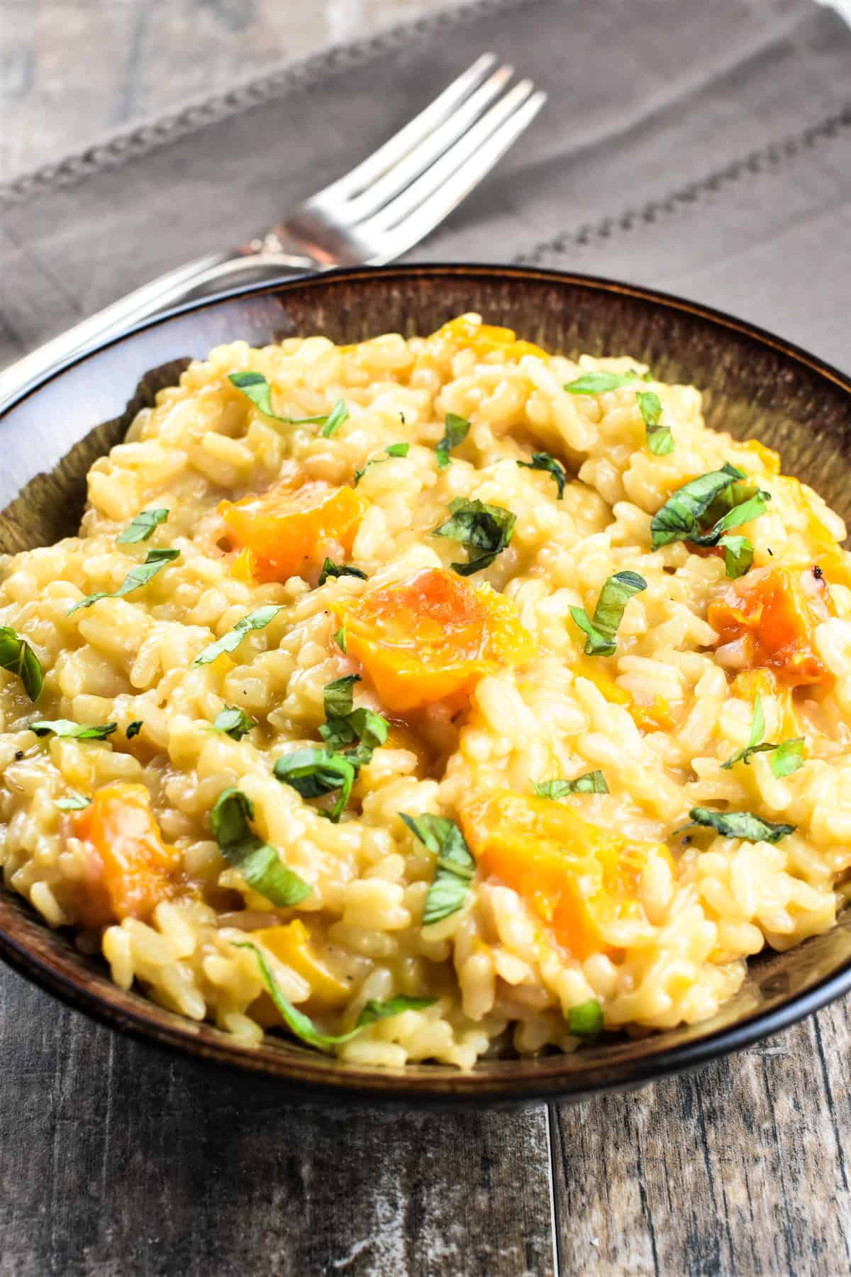 Butternut squash risotto in a bowl on a kitchen napkin with a fork behind it.