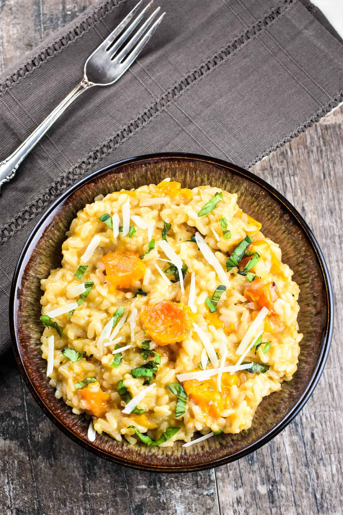 Butternut squash risotto in a bowl garnished with Parmesan and fresh herbs.