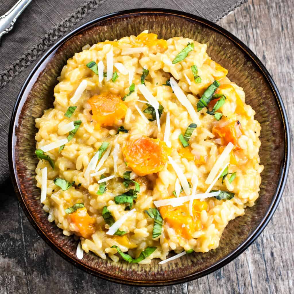 Close-up of butternut squash risotto in a bowl garnished with fresh basil and parmesan cheese.