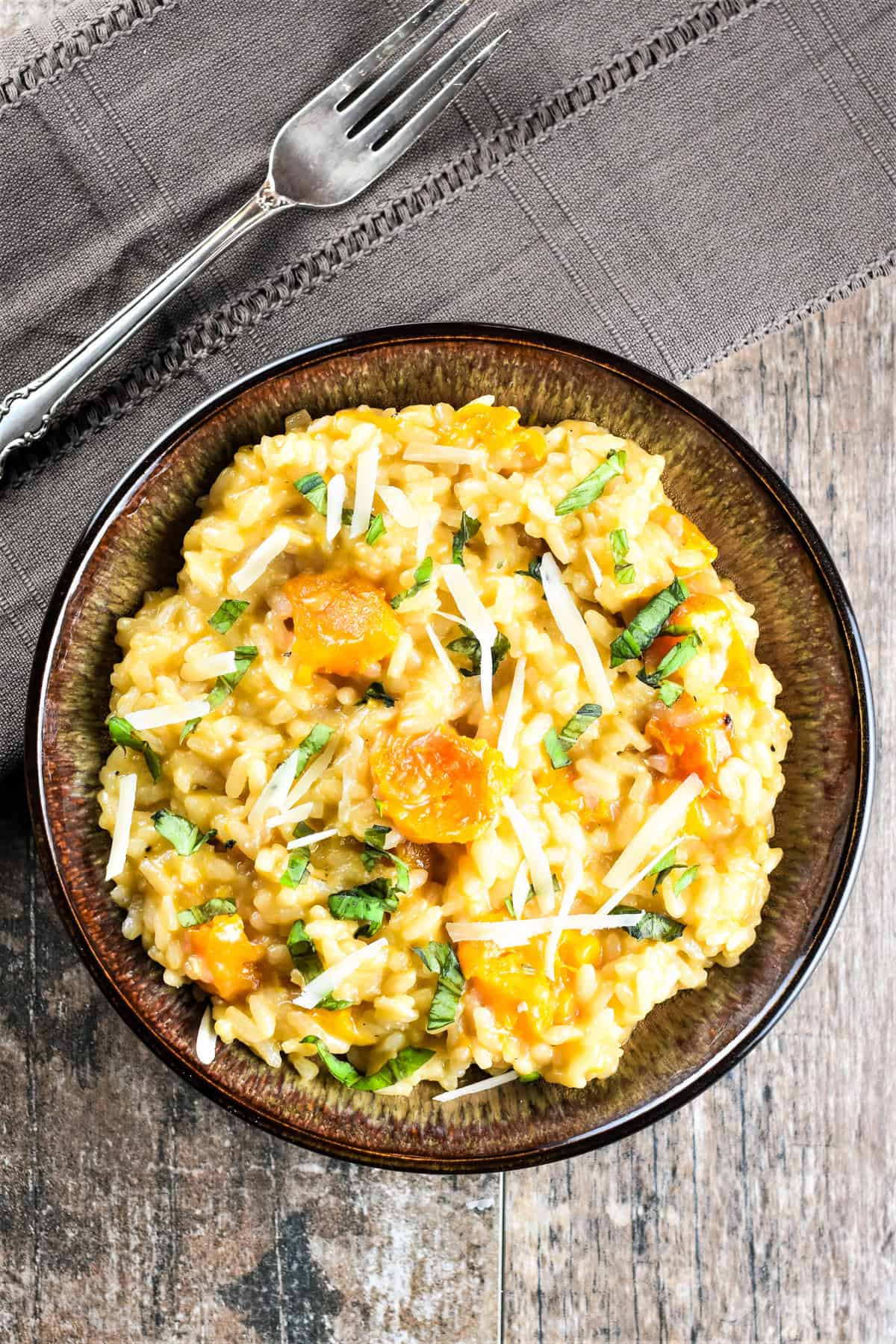 Butternut squash risotto garnished with fresh basil and parmesan cheese in a bowl.