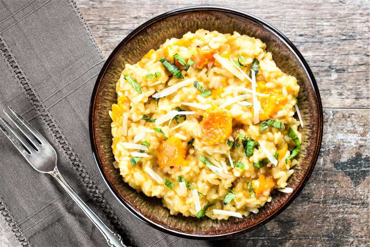 Butternut squash risotto in a bowl with a fork on a kitchen napkin next to it.