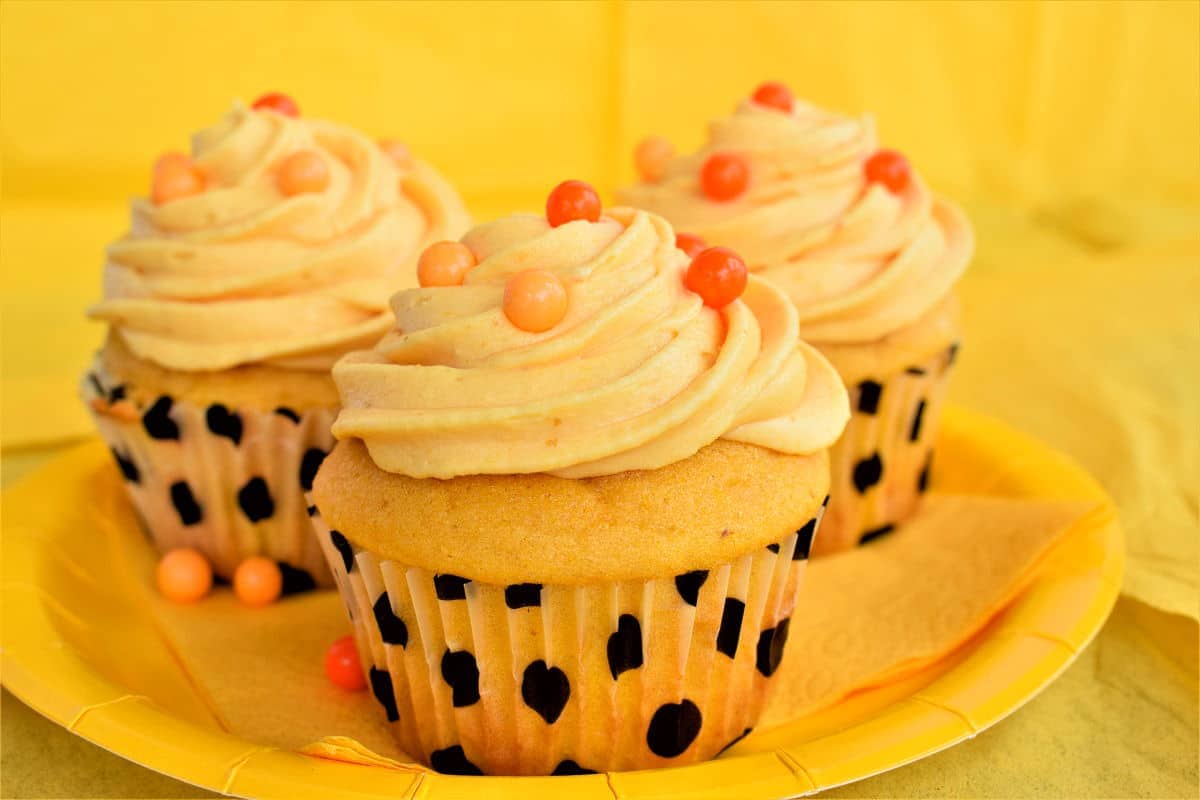 Three pumpkin cupcakes on a yellow plate.