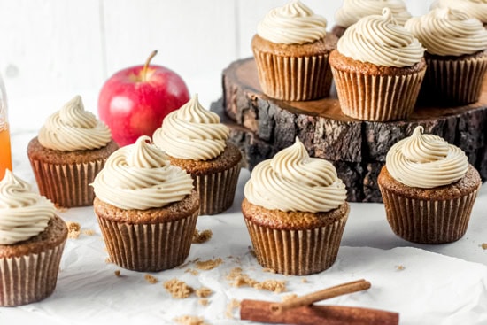 Apple cider cupcakes with cinnamon sticks in the front and an apple behind them.