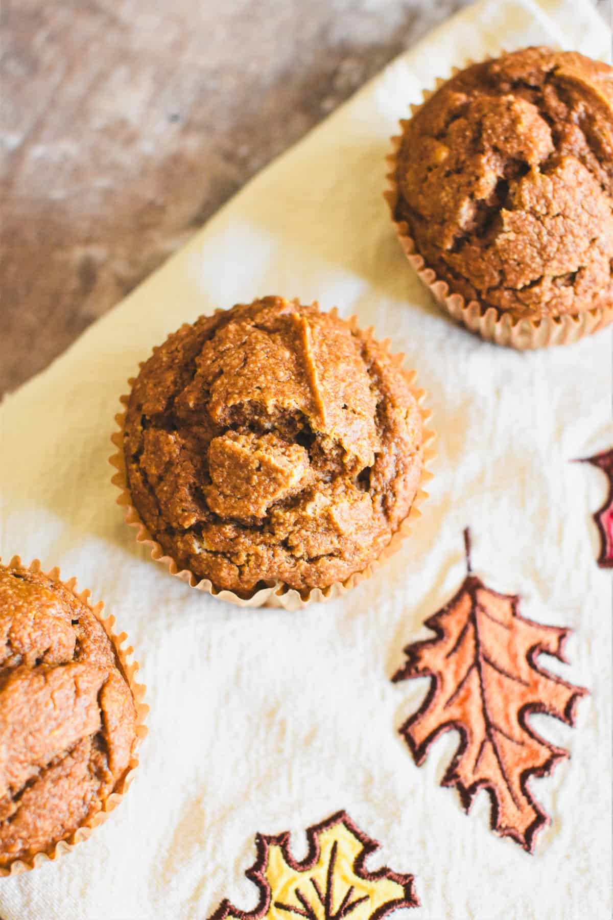 Oat flour pumpkin muffins on a kitchen towel with a fall leaves print.